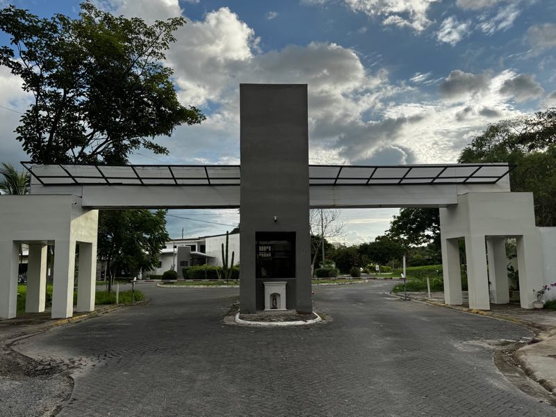 Pórtico de entrada del condominio con la caseta de control al centro y la calle adoquinada